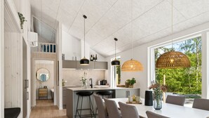 Une cuisine moderne dotée d’un îlot central, de luminaires suspendus et offrant une vue sur la verdure environnante.