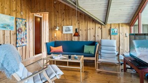 Een knus interieur met houten wanden, een blauwe bank, een witte fauteuil, een glazen salontafel en een televisie.