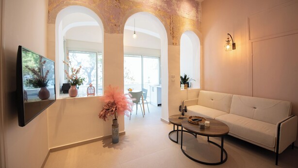 Un salon moderne avec un canapé blanc, une table basse et un téléviseur fixé au mur. On y trouve des portes en arc de cercle et une grande fenêtre qui laisse entrer la lumière naturelle.
