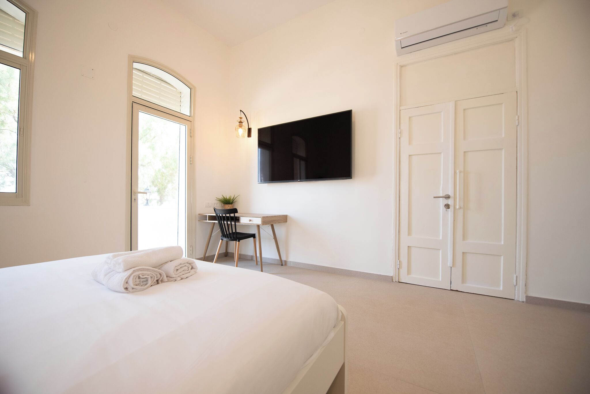 A bedroom with a bed, a desk, a chair, a TV, and a door.