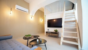 Un salon moderne avec un canapé, une table basse, un téléviseur et une échelle en bois menant à une mezzanine.