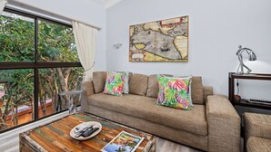 A living room with a large window, a sofa with tropical pillows, a wooden coffee table with magazines and a remote, and a map on the wall. - San Lameer Villa 2849 (Southbroom)