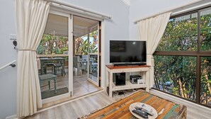 A room with a TV on a wooden stand, a table with remote controls, and a sliding glass door leading to an outdoor area with chairs and a table. - San Lameer Villa 2849 (Southbroom)