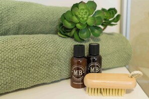 Une surface verte texturée avec deux bouteilles étiquetées « MB » et une brosse en bois.