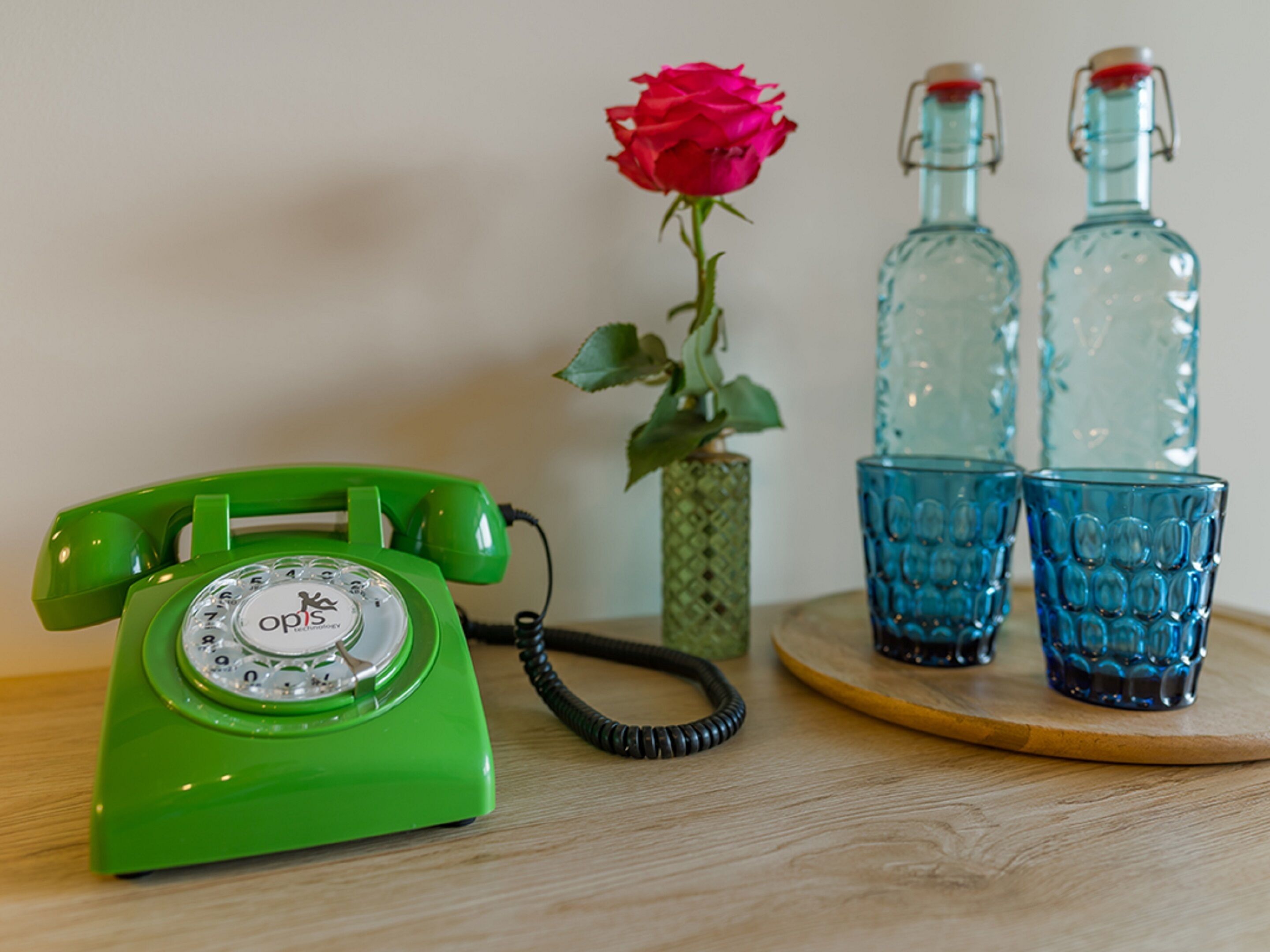 A green rotary dial telephone, a red rose, and two blue glass bottles on a wooden surface.