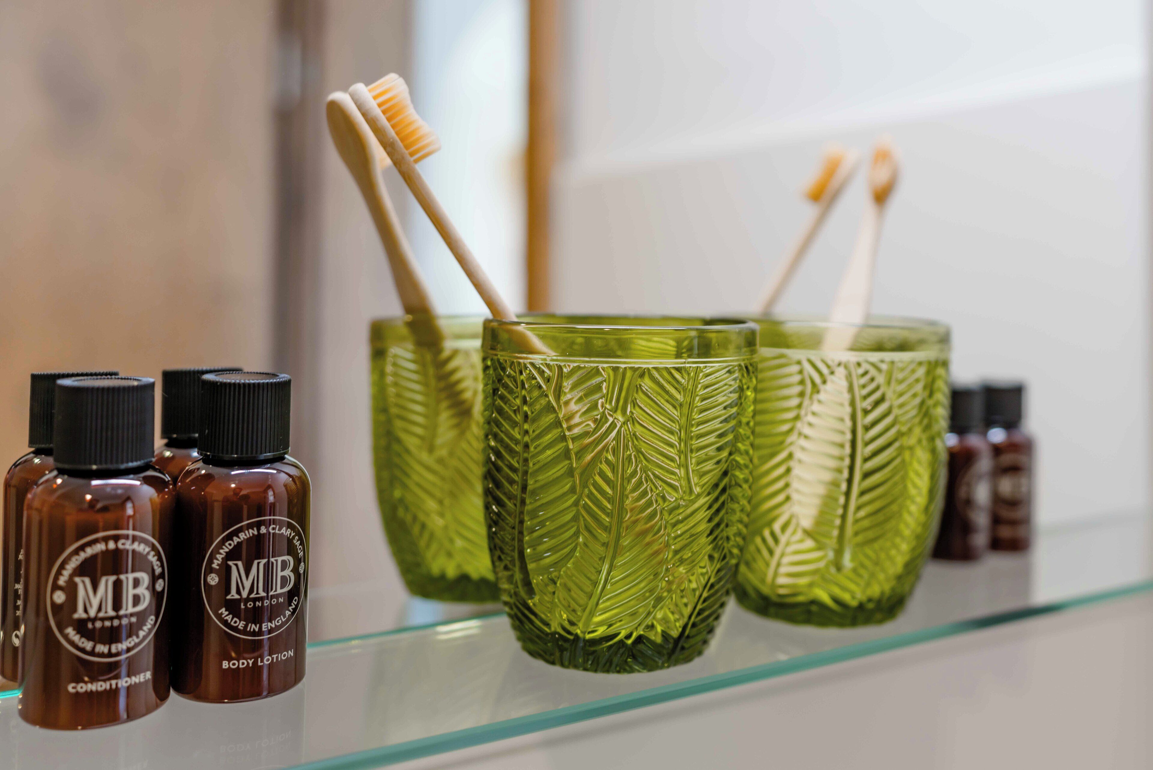 Ein Badezimmerschrank mit grünen Gläsern, zwei Körperlotionflaschen und zwei Zahnbürsten.