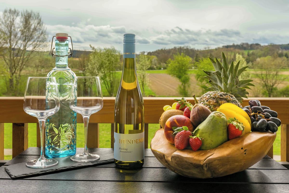 A wooden table with a bottle of wine, two glasses, and a bowl of fruit.