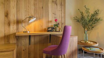 A wooden desk with a lamp, a chair, a small table with a vase and a plant, and a wall with vertical wooden panels.