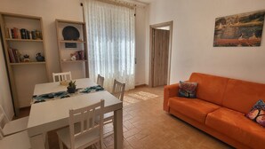 A living room with a white table, orange sofa, and a painting on the wall. - Accogliente Appartamento, Animali Ammessi, Vicino Roma, Bracciano, Ladispoli (Lazio)