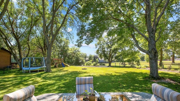 A backyard with a glass table, two striped chairs, and a swing set.
