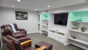 A modern living room with a leather recliner, wooden coffee table, and a flat-screen TV on a white entertainment unit.
