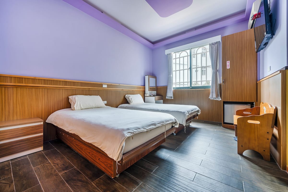 Una habitación con dos camas, un banco de madera, un televisor y una ventana con cortinas.