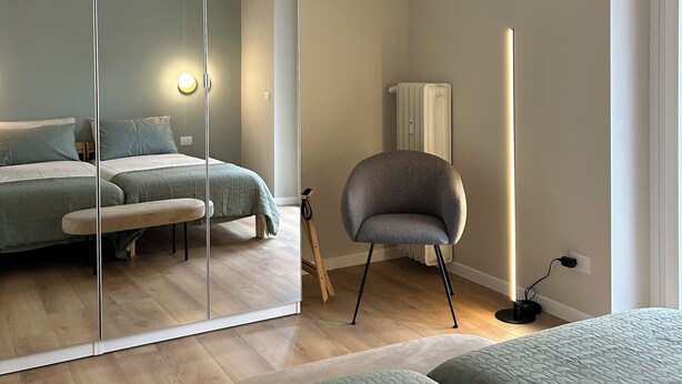 Une chambre avec un grand miroir, deux lits, une chaise et une lampe sur pied.