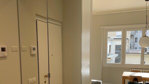 Une pièce dotée d’une armoire aux portes miroir, d’un coin repas avec une table et des chaises, et d’une fenêtre donnant sur des immeubles.