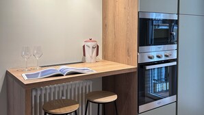 Une cuisine moderne équipée d’un four encastré, d’une machine à café et de deux tabourets.