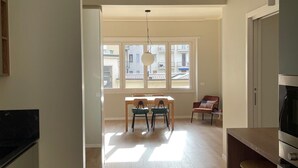 Une cuisine moderne avec un plancher en bois, un coin repas comprenant une table et des chaises, et une grande fenêtre laissant entrer la lumière naturelle.