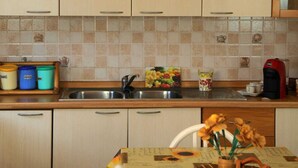 A kitchen with light-colored cabinets, a tiled backsplash, a sink, and a dining table with a sunflower tablecloth. - Relax in Style:Spacious 4-Bedroom Villa Rosetta Near Palermo's Coastal Treasures (Carini)