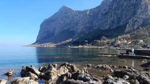 A coastal landscape with rocky terrain, clear water, and a mountain in the background. - Relax in Style:Spacious 4-Bedroom Villa Rosetta Near Palermo's Coastal Treasures (Carini)