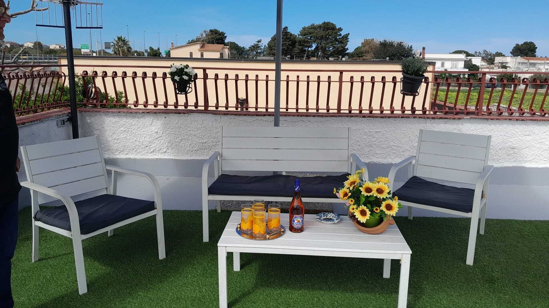 Un espace patio avec des chaises et une table en métal blanc, une bouteille de bière et un vase rempli de tournesols.