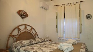 A bedroom with a bed, a bedside table, a wall-mounted air conditioner, and a window with curtains. - Relax in Style:Spacious 4-Bedroom Villa Rosetta Near Palermo's Coastal Treasures (Carini)