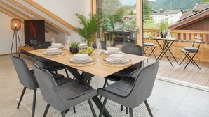 Ein Essbereich mit einem Holztisch, gedeckt für sechs Personen, umgeben von grau gepolsterten Stühlen. Auf dem Tisch stehen ein Blumentopf und ein kleiner Tisch mit einer Glasvase.