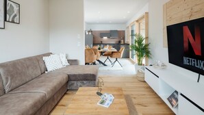 A modern living room with a brown sofa, a wooden coffee table, and a flat-screen TV mounted on the wall.