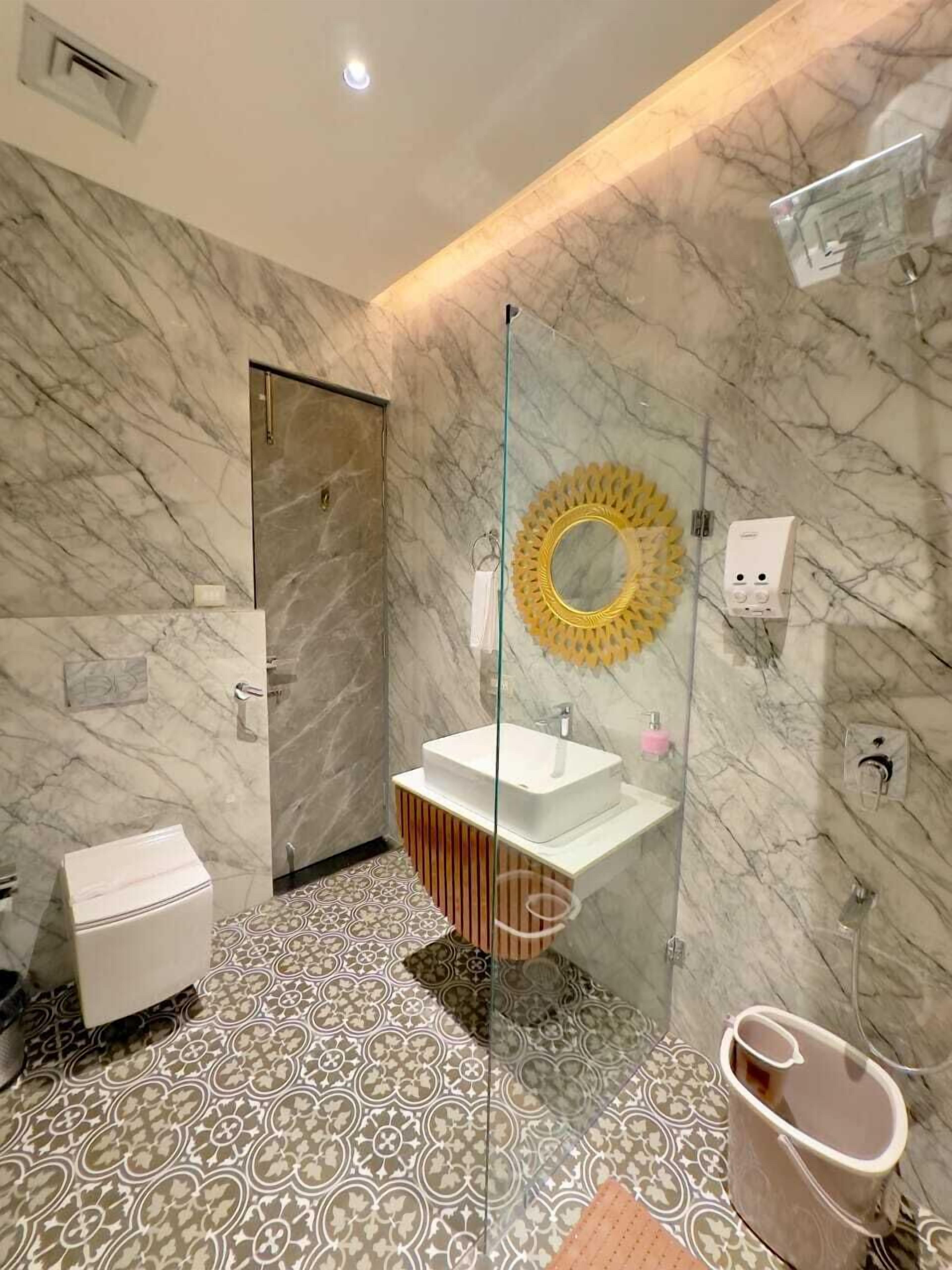 A bathroom with a marble wall, a glass-enclosed sink, a toilet, and a shower area.