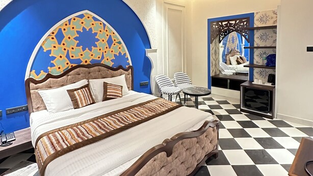 Una habitación de hotel moderna con una cama grande, un ventilador de techo, una pared con diseño y un suelo a cuadros.