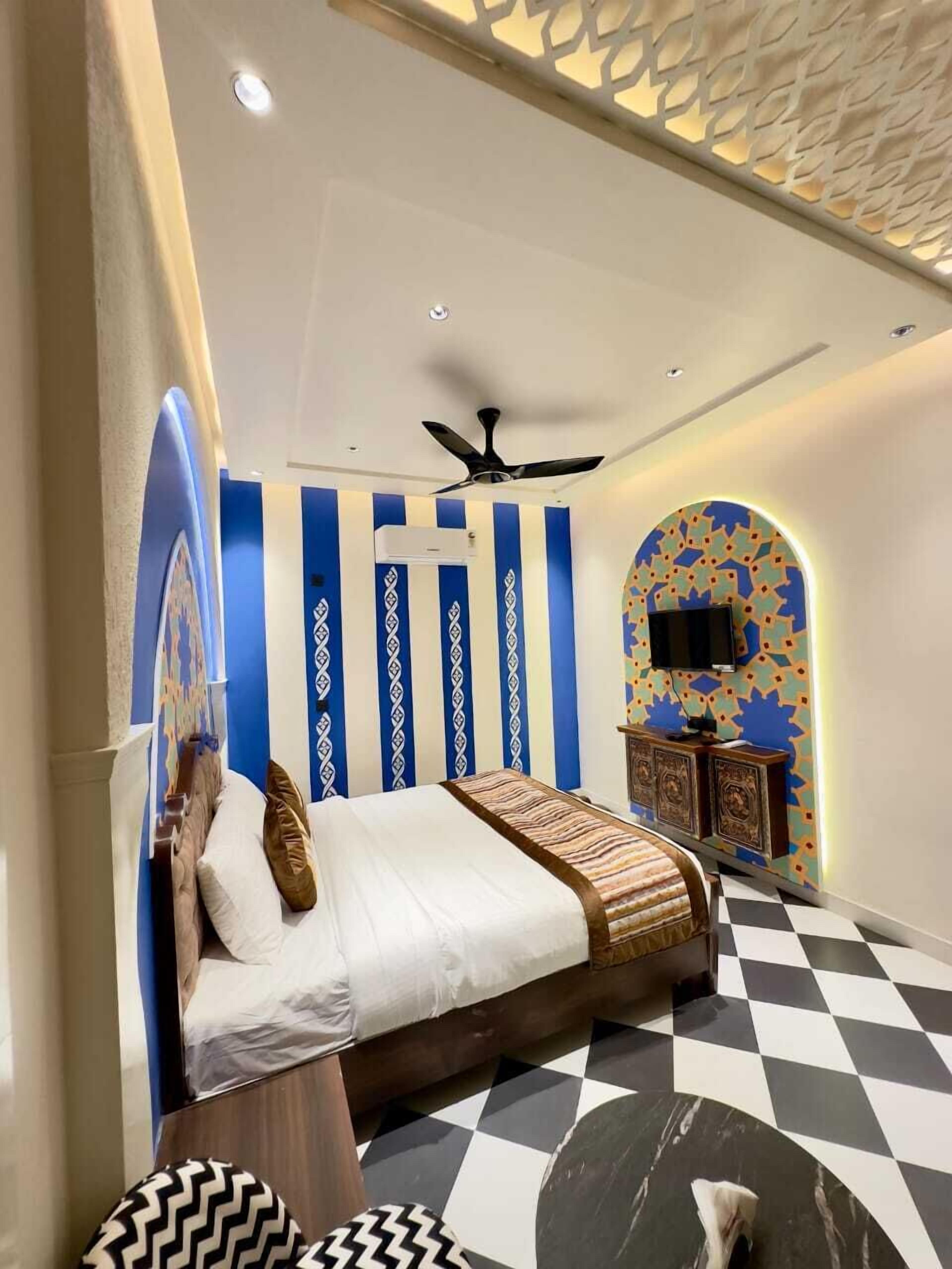 A bedroom with a bed, a ceiling fan, a TV, and a patterned wall.