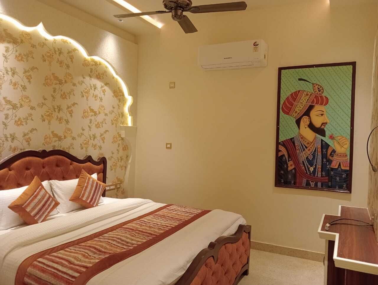 A bedroom with a large bed, a ceiling fan, an air conditioning unit, and a wall-mounted painting.