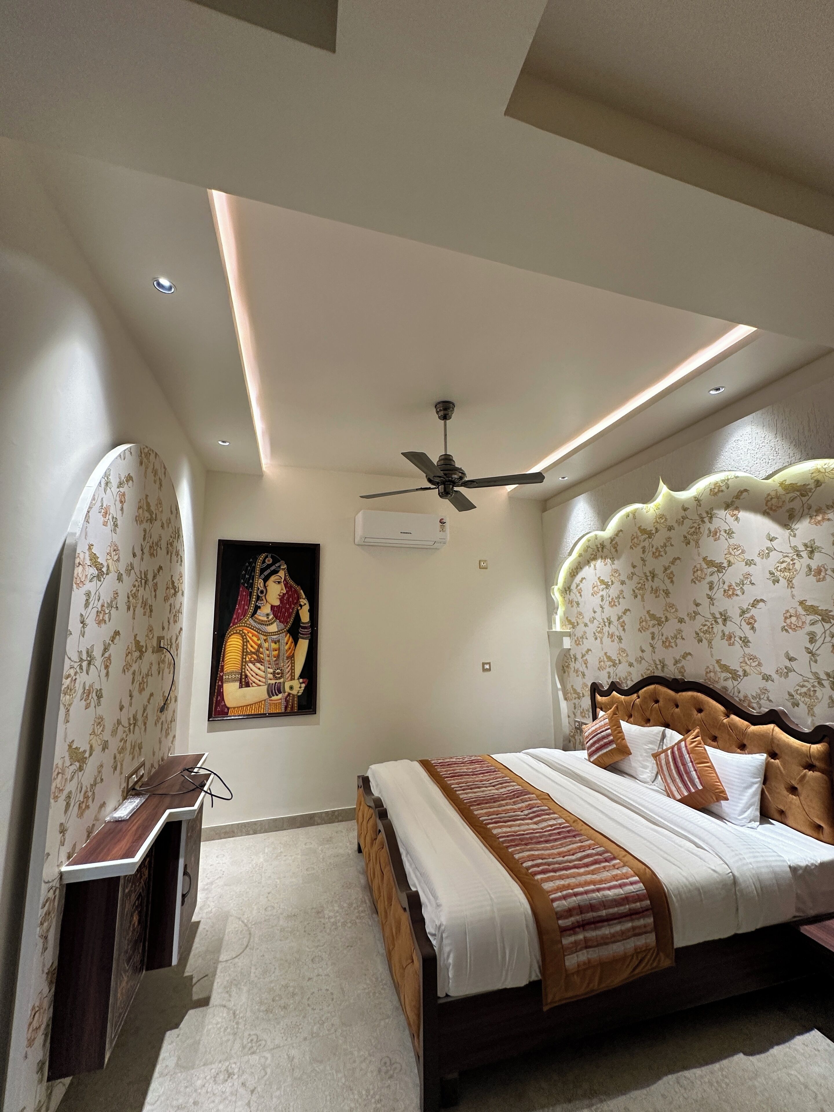 A bedroom with a bed, a ceiling fan, an air conditioning unit, and a decorative painting on the wall.