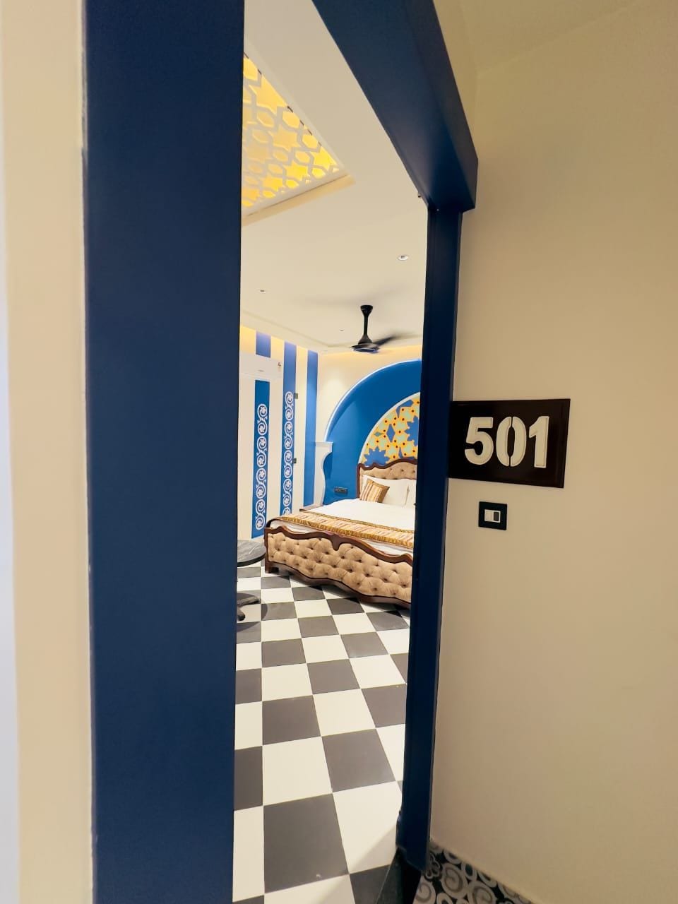 Ein Hotelzimmer mit Schachbrettmuster-Boden, einem Bett mit floralem Kopfteil und einem Schild mit der Zimmernummer 501.