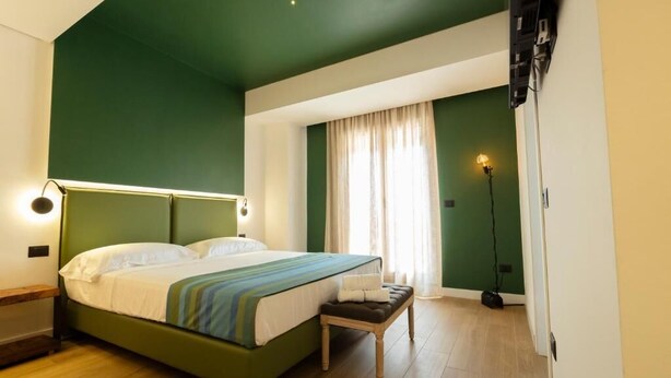 A bedroom with a green bed, a bedside table, a bench, a floor lamp, and a window with curtains. - Master bedroom with terrace (San Costantino di Briatico)