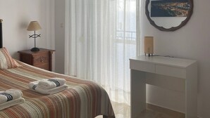 A bedroom with a bed, a desk, an air conditioner, a lamp, a mirror, and a view of a cityscape through a window. - Casa Blue in Torrox With 2 Bedrooms and 1 Bathrooms (Torrox)