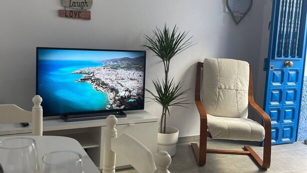 A living room with a television displaying a coastal scene, a chair, a potted plant, and a wall with motivational signs. - Casa Blue in Torrox With 2 Bedrooms and 1 Bathrooms (Torrox)
