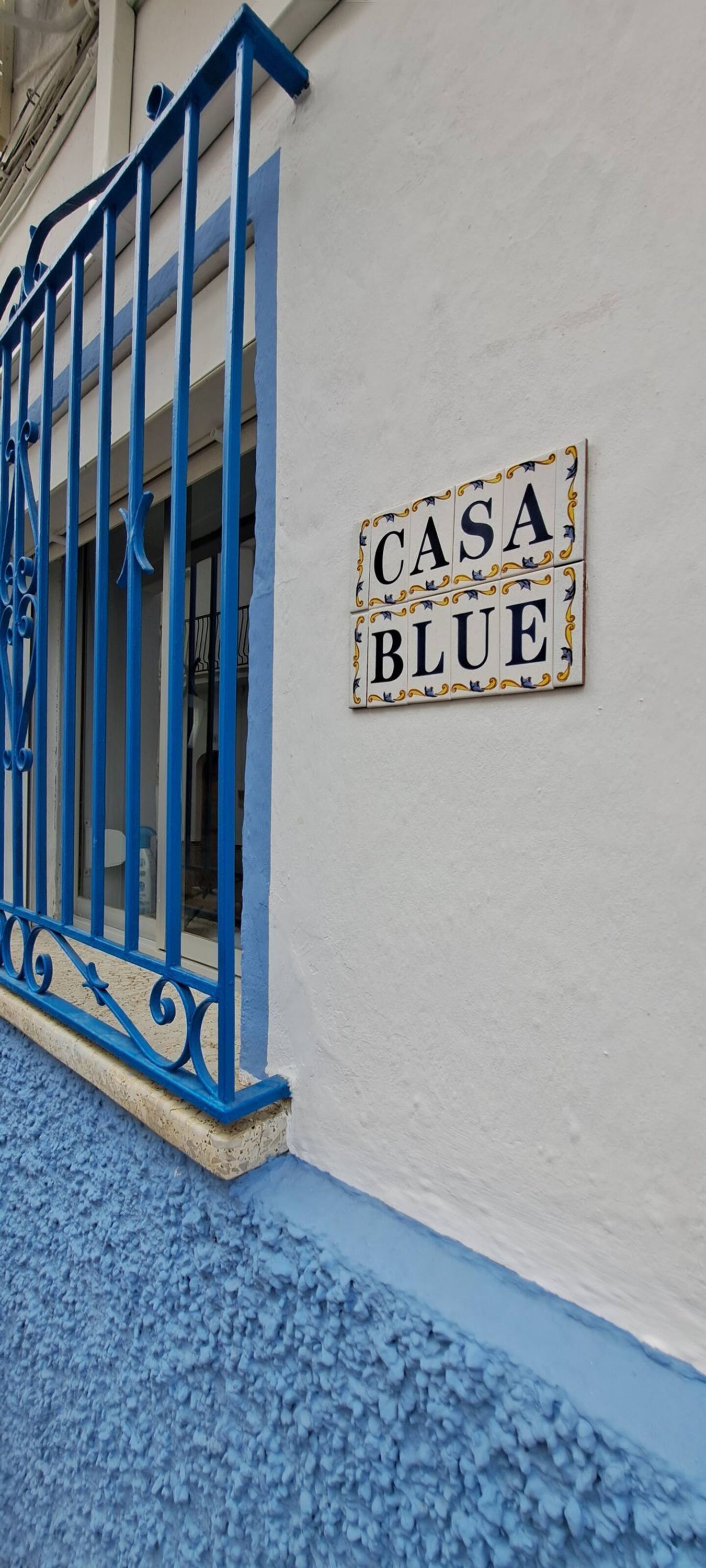 Une façade d’immeuble aux couleurs bleu et blanc, une porte en métal et une enseigne indiquant « CASA BLUE ».