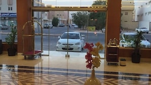 En hotelllobby med en entré av glas, ett marmorgolv och en vas med blommor.