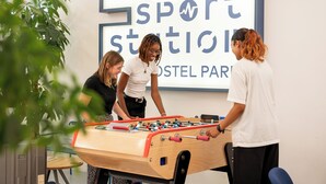 A foosball table in a room with a large sign reading "UCPA Sport Station" and a plant in the foreground. - UCPA Sport Station Hostel Paris (Paris)