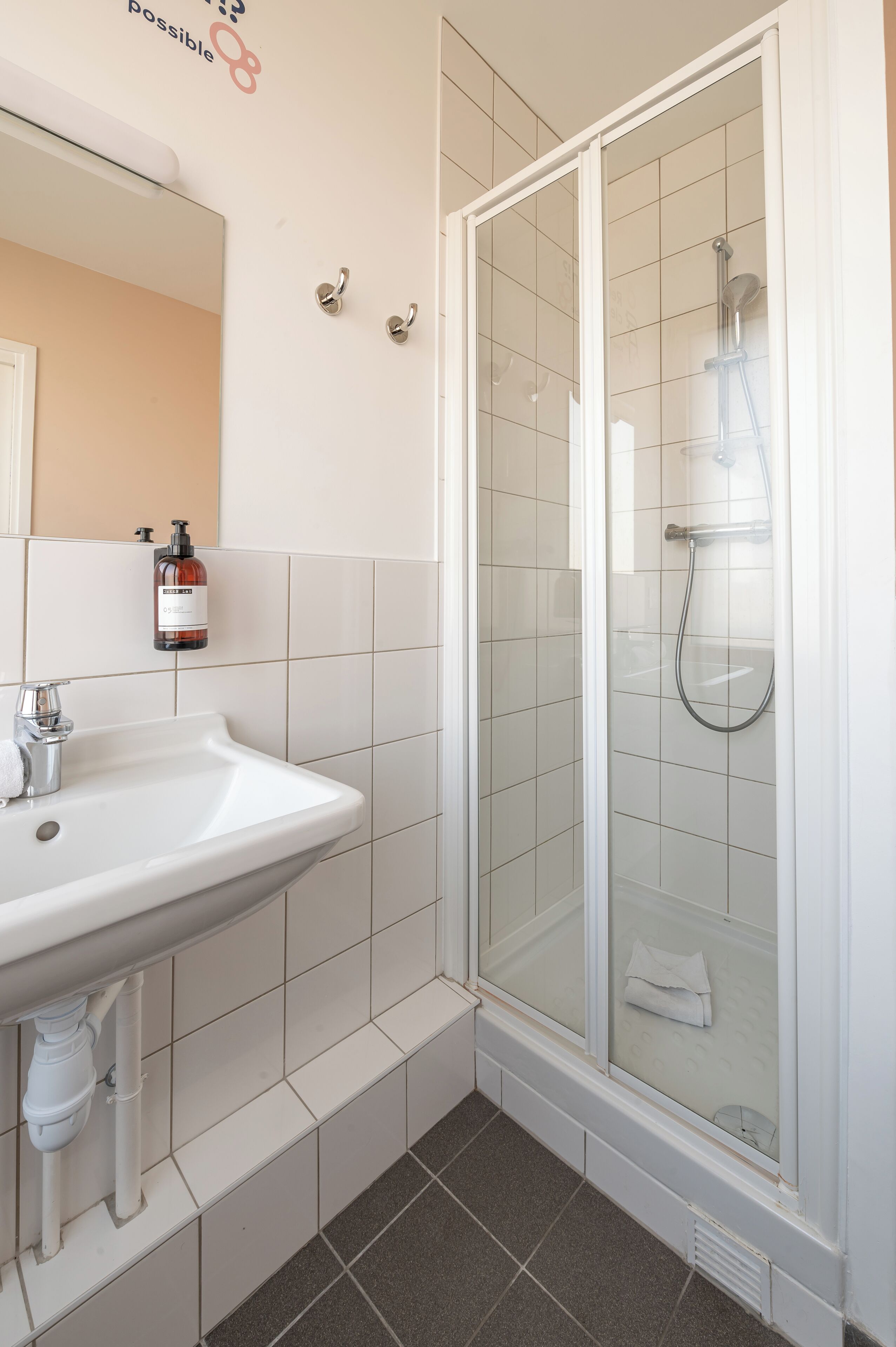 A bathroom with a white sink, a glass shower enclosure, and a mirror with a towel hanging on it.