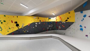 An indoor climbing wall with various colored holds and a white padded area. - UCPA Sport Station Hostel Paris (Paris)