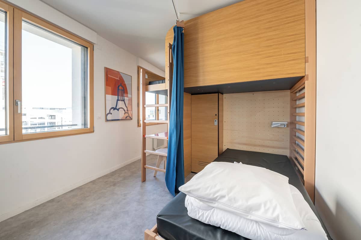 Ein kleines Zimmer mit einem Etagenbett, einem Fenster und einer Tür zu einem weiteren Raum.