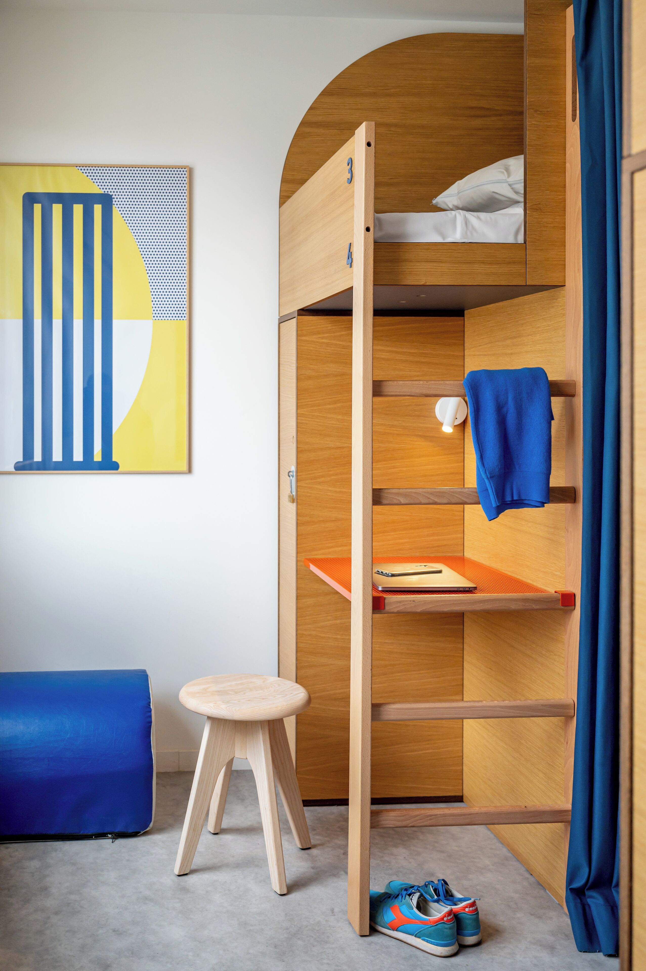 A bunk bed with a desk and a chair, a blue curtain, and a pair of shoes on the floor.