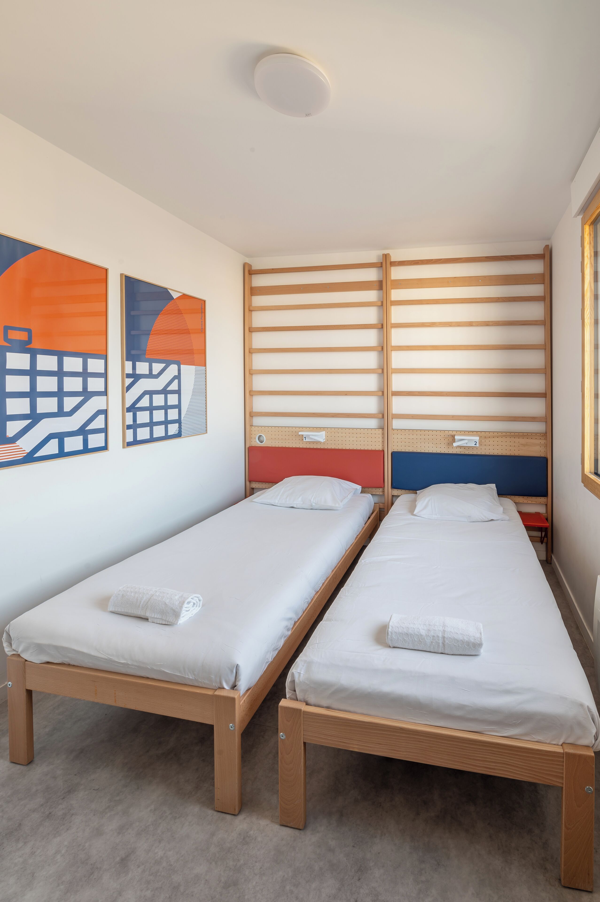 A room with two single beds, wooden headboards, and a cityscape artwork on the wall.