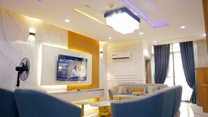 A modern living room with a flat-screen TV mounted on the wall, a sofa, a coffee table, and a fan. - Luxury 3 bedroom, Secure, Water View, 24/7 Power in secluded estate - Ikoyi  (Lagos)