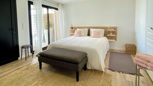 A modern bedroom with a large bed, a bench, and a view of the outdoors. - Apartment TY COSY in front of the beach of the blocked fort, calm and serenity.  (Ploemeur)