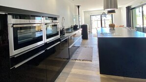 A modern kitchen with built-in ovens, a central island, and a large window providing natural light. - Apartment TY COSY in front of the beach of the blocked fort, calm and serenity.  (Ploemeur)