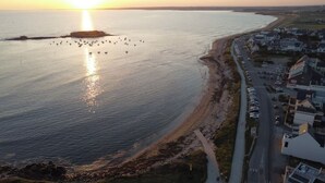 An aerial view of a coastal town with a beach, a road, and buildings along the shore. - Apartment TY COSY in front of the beach of the blocked fort, calm and serenity.  (Ploemeur)