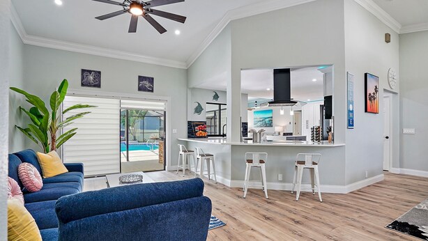Un salon moderne avec un canapé bleu, un ventilateur de plafond et un coin cuisine équipé de tabourets de bar.