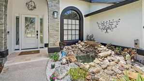 Une maison avec une façade en pierre, une porte blanche et un petit jardin agrémenté de rochers et de plantes.