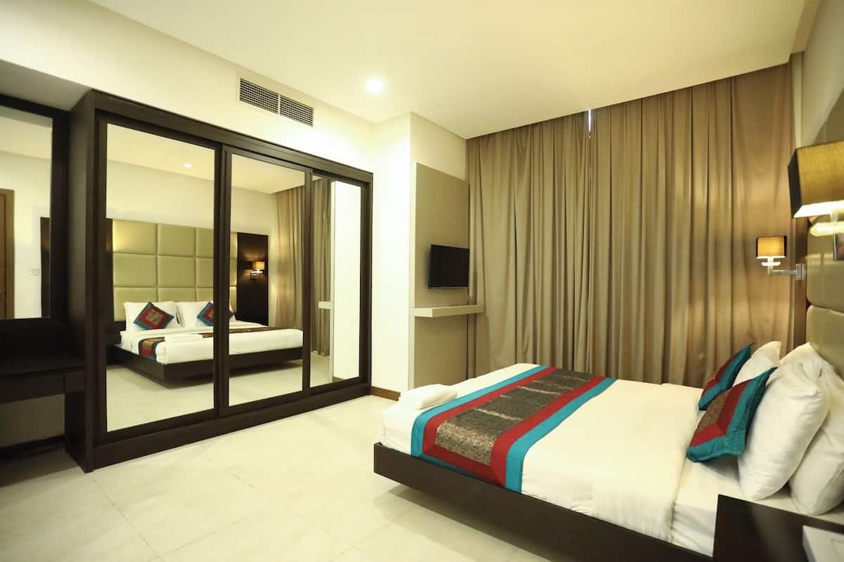 A hotel room with a large bed, a mirror, a television, and a sliding door leading to another room.